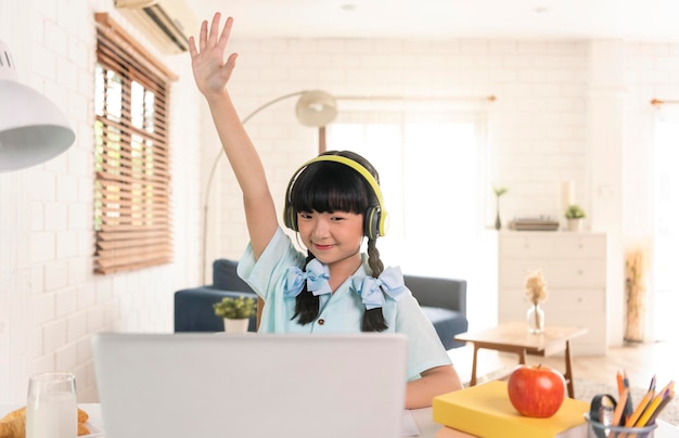 Niña asiática que usa una computadora portátil para estudiar en línea la educación en el hogar durante la cuarentena en el hogar