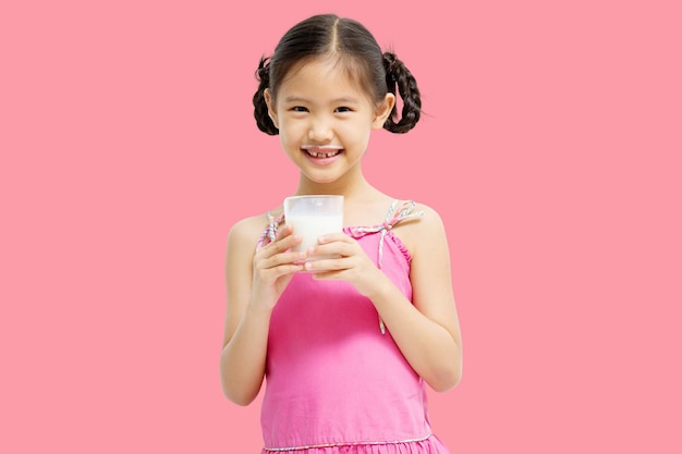 Niña asiática sonriente bebiendo leche aislada de fondo rosa