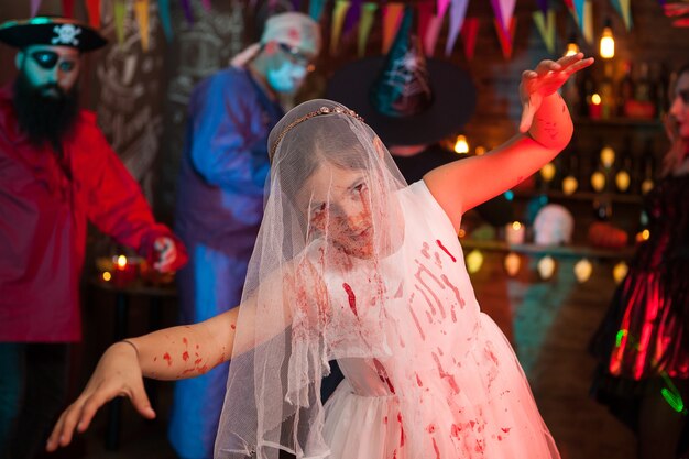 Niña asustadiza en una fiesta de Halloween vestida como una novia con vestido de deshierbe. Pirata aterrador en el fondo.