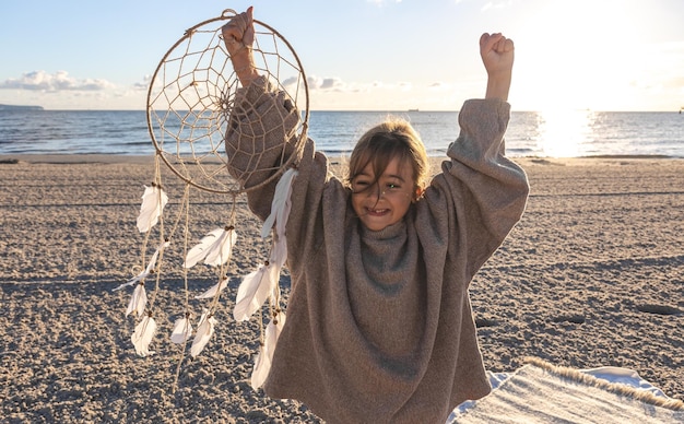 Foto gratuita niña con un atrapasueños en la orilla del mar al atardecer