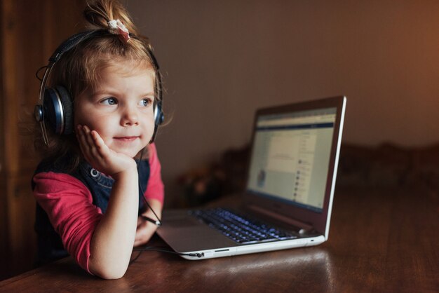 Niña con auriculares escuchando música, usando una computadora portátil