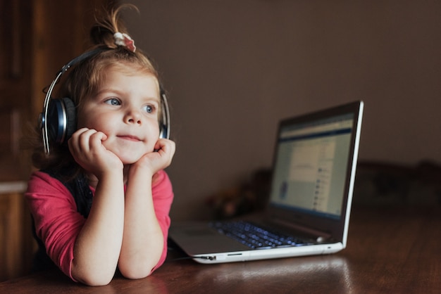 Niña con auriculares escuchando música, usando una computadora portátil