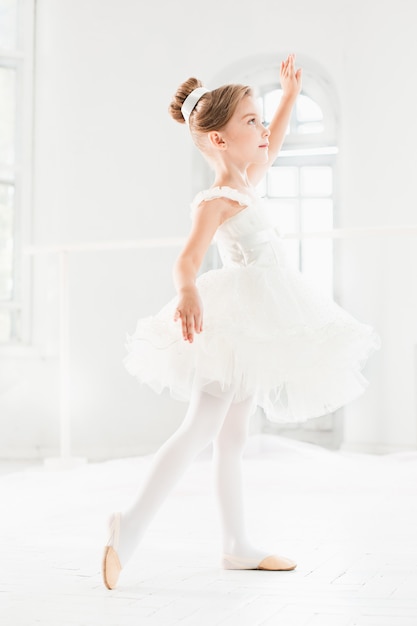 Niña bailarina en un tutú. Adorable niño bailando ballet clásico en un estudio blanco.