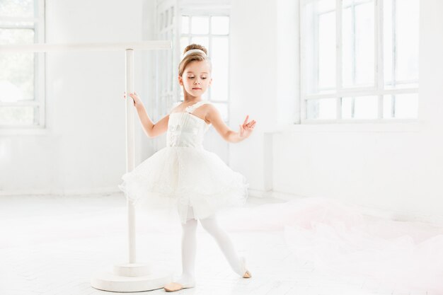 Niña bailarina en un tutú. Adorable niño bailando ballet clásico en un estudio blanco.