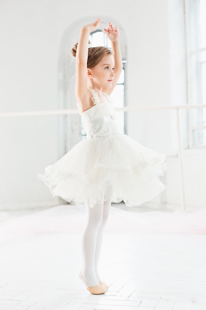 Niña bailarina en un tutú. Adorable niño bailando ballet clásico en un estudio blanco.