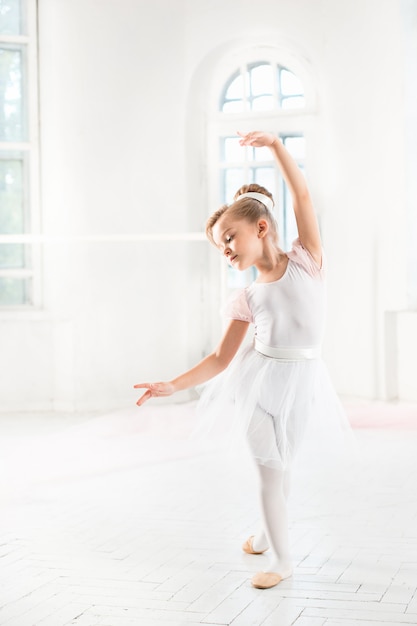 Niña bailarina en un tutú. Adorable niño bailando ballet clásico en un estudio blanco.