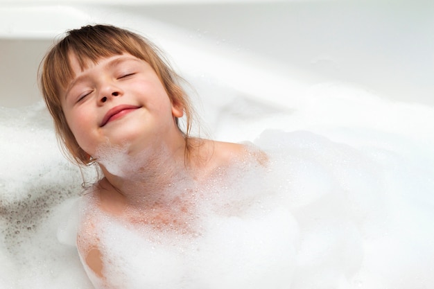 Vista lateral de una niña bañándose en la bañera | Foto Gratis
