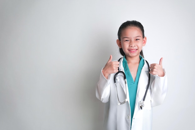 Foto gratuita una niña en una bata de laboratorio con un estetoscopio dando los pulgares hacia arriba.