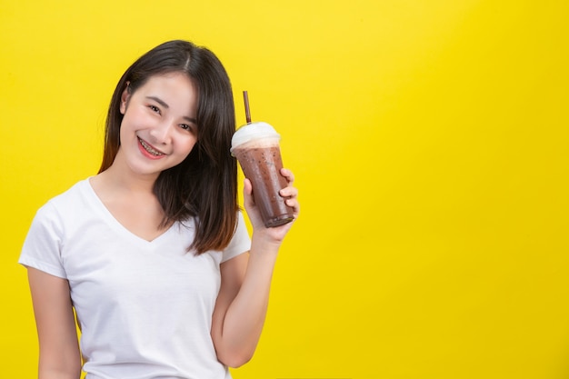 La niña bebe agua fría del cacao de un vaso de plástico transparente en un amarillo.