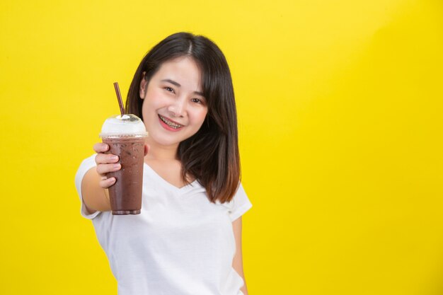 La niña bebe agua fría del cacao de un vaso de plástico transparente en un amarillo.