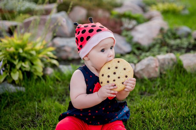 Niña bebé con una gran galleta de chocolate se sienta en el patio trasero