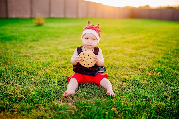 Niña bebé con una gran galleta de chocolate se sienta en el patio trasero