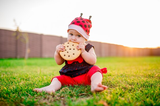 Niña bebé con una gran galleta de chocolate se sienta en el patio trasero