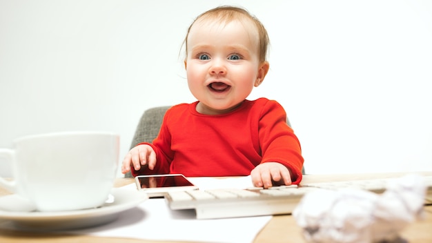 Niña bebé sentado con el teclado de la computadora moderna o portátil en el estudio blanco.