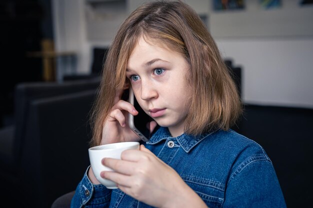 Niña bebe té y parece sorprendida hablando por teléfono