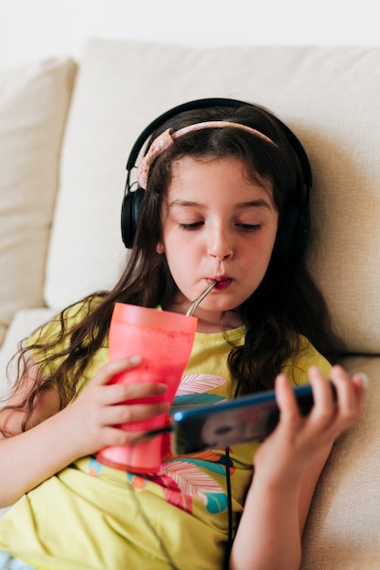 Niña bebiendo jugo y mirando el teléfono