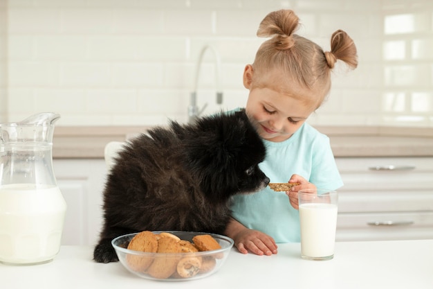 Niña bebiendo leche y jugando con perro en casa