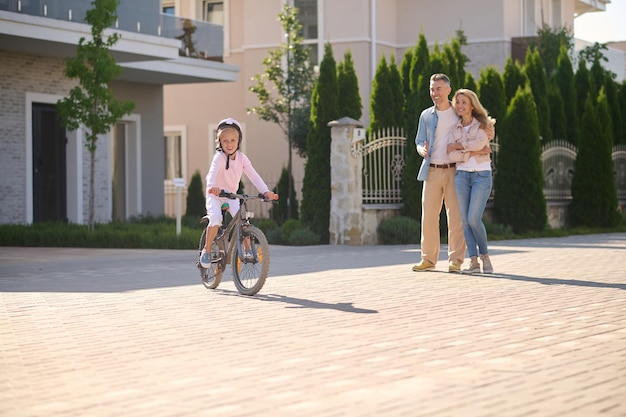 Una niña en bicicleta mientras sus padres la miran.