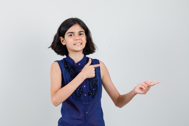 Niña en blusa azul apuntando hacia el lado derecho y mirando juguetón