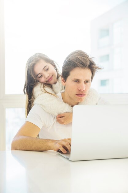 Niña bonita abrazando a su padre trabajando en la computadora portátil en casa