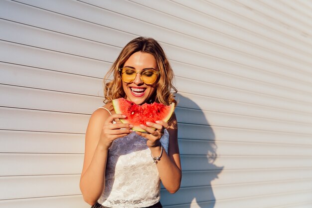 Niña bonita comiendo una sandía, con gafas de sol amarillas, disfrutando de los días de verano