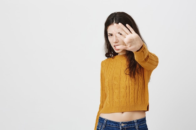 Niña bonita disgustada y molesta extiende la mano para rechazar o dejar de fotografiar, no le gusta tomar fotografías de sí misma