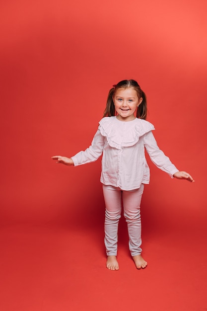 Niña bonita se divierte mucho en el estudio fotográfico, imagen aislada sobre fondo rojo