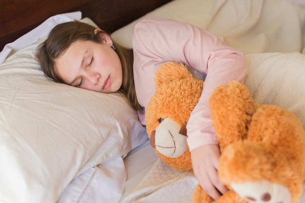 Niña bonita durmiendo con oso de peluche en la cama