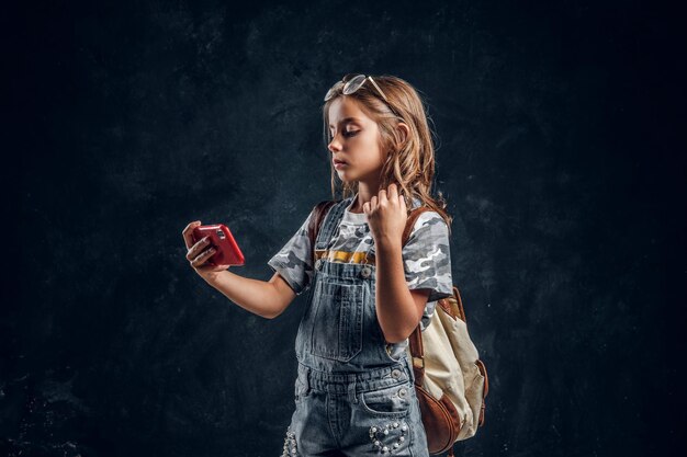 Una niña bonita se está haciendo selfie por teléfono móvil en un estudio fotográfico oscuro.