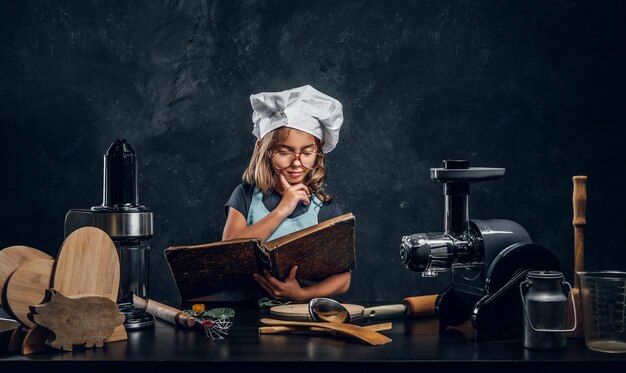 La niña bonita está leyendo un libro de recetas y tiene una gran idea de qué cocinar para la cena.