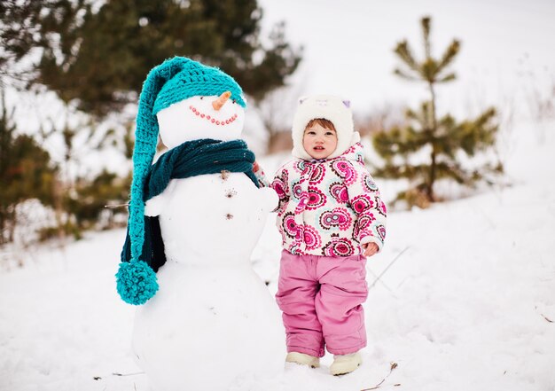 Una niña bonita está de pie junto a un sonriente muñeco de nieve.