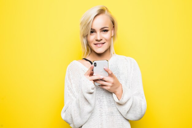 Niña bonita joven mujer en suéter blanco utiliza smartphone en amarillo