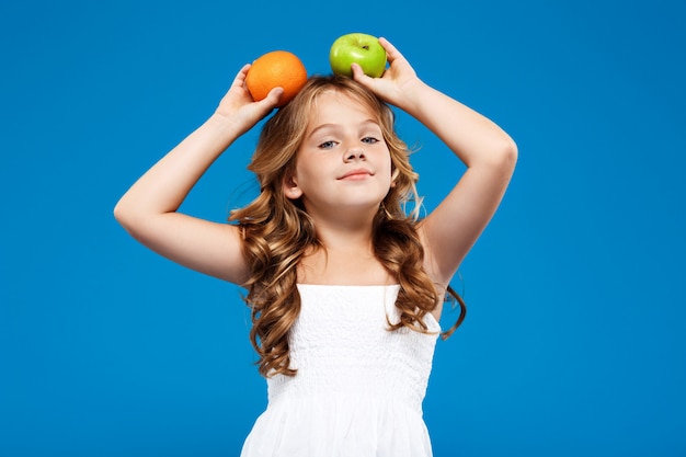 Foto gratuita niña bonita con manzana y naranja sobre pared azul