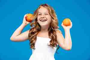 Foto gratuita niña bonita con naranjas, sonriendo sobre la pared azul