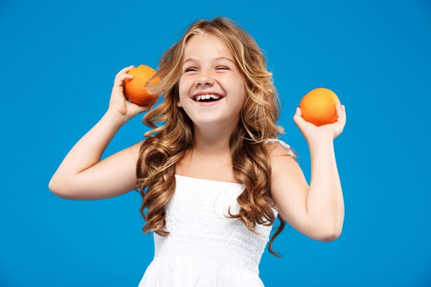 Niña bonita con naranjas, sonriendo sobre la pared azul