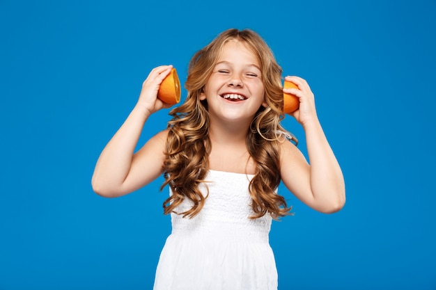 Niña bonita con naranjas, sonriendo sobre la pared azul