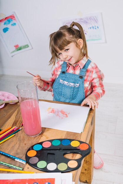 Niña bonita pintando con acuarela sobre papel.