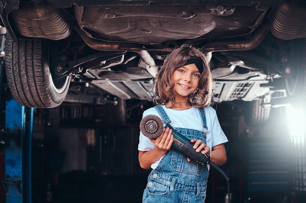 Foto gratuita la niña bonita posa para el fotógrafo con una herramienta en el taller de autoservicio.