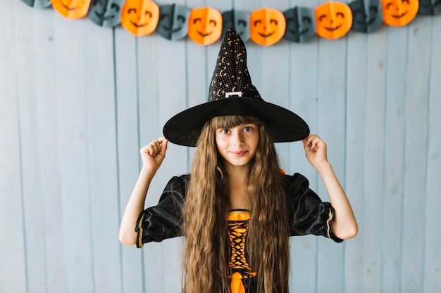 Foto gratuita niña bonita con sombrero de bruja y sonriendo en la fiesta de halloween