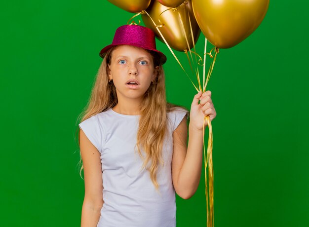 Niña bonita con sombrero de fiesta con montón de globos