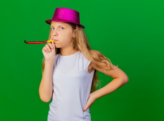 Niña bonita con sombrero de fiesta que sopla el silbato celebrando un cumpleaños