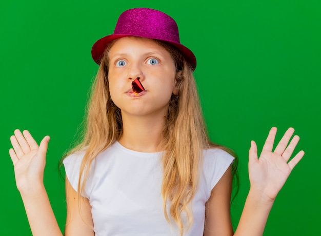 Niña bonita con sombrero de fiesta que sopla el silbato