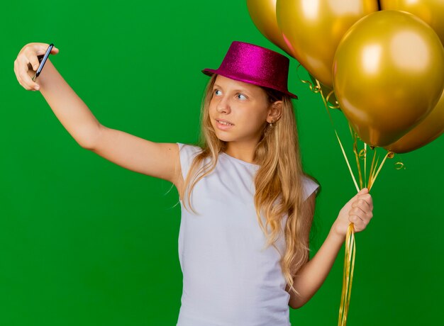 Niña bonita con sombrero de fiesta con smartphone