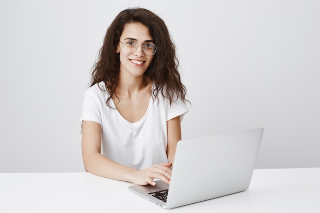 Niña bonita sonriente con gafas usando laptop