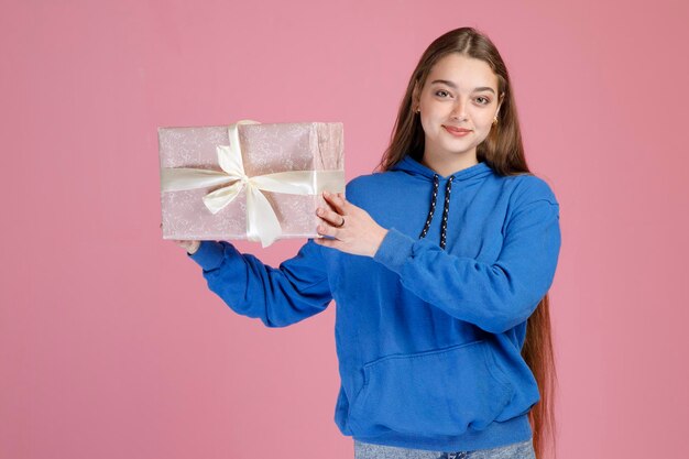 Niña bonita sonriente con el pelo largo que muestra un bonito regalo decorado mientras mira a la cámara