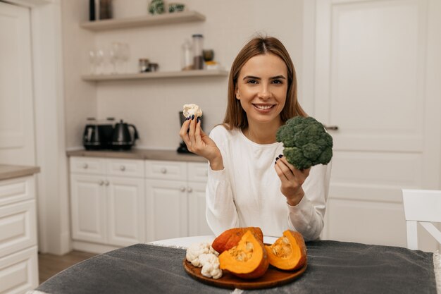 Niña bonita sonriente preparándose para cocinar con verduras en la cocina