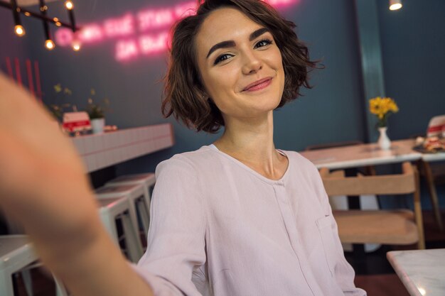 Niña bonita sonriente tomando un selfie en un café