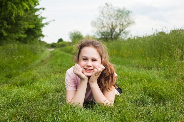 Niña bonita sonriente tumbado en la hierba verde en el parque