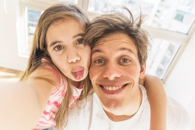 Niña bonita con su padre tomando selfie divertido