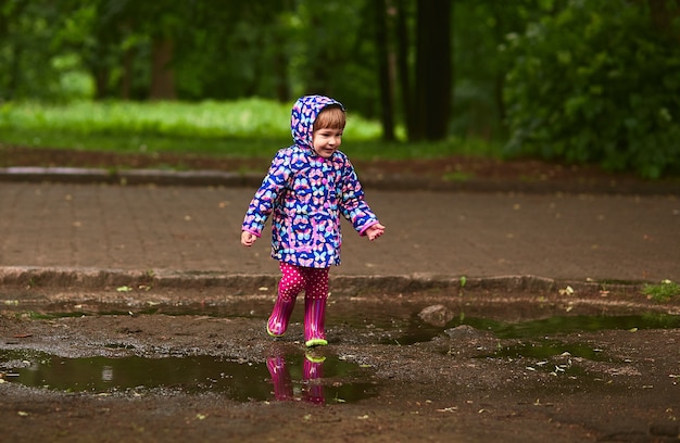 Niña en botas de goma se divierte caminando en las piscinas después de la lluvia